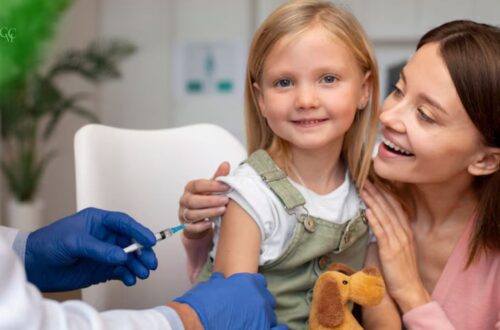 Bebê sorrindo com um adesivo de curativo no braço após vacinação, com uma enfermeira sorrindo ao fundo, simbolizando a proteção da vacinação infantil.
